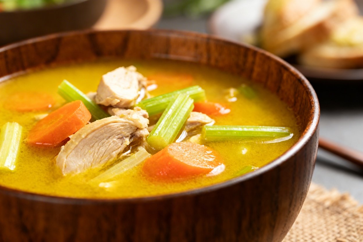30–45 degrees, focusing on details to emphasize the texture of the turmeric chicken soup in the dark